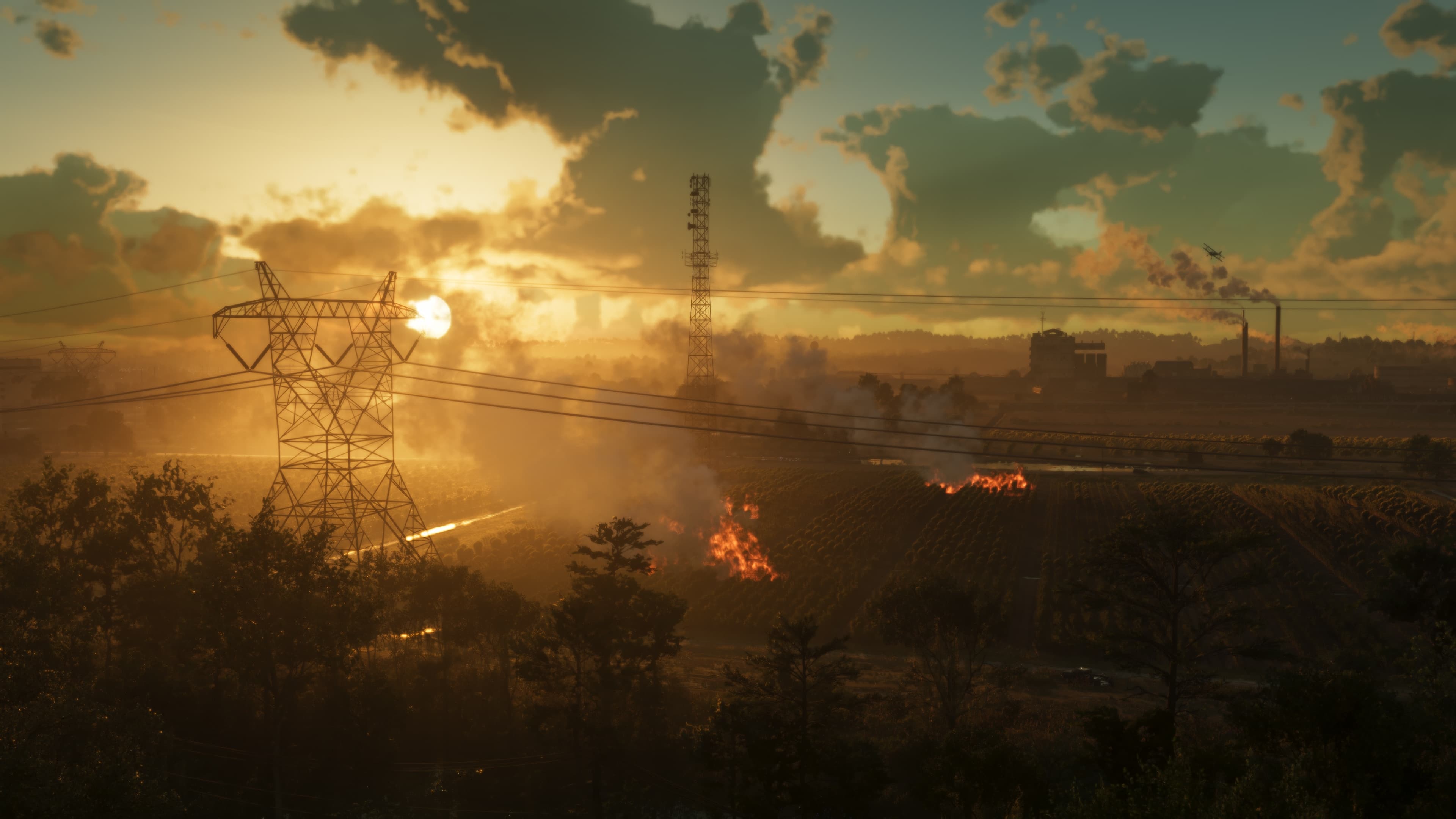 Sunset over marshland with transmission pylons silhouetted and fires burning on the far bank