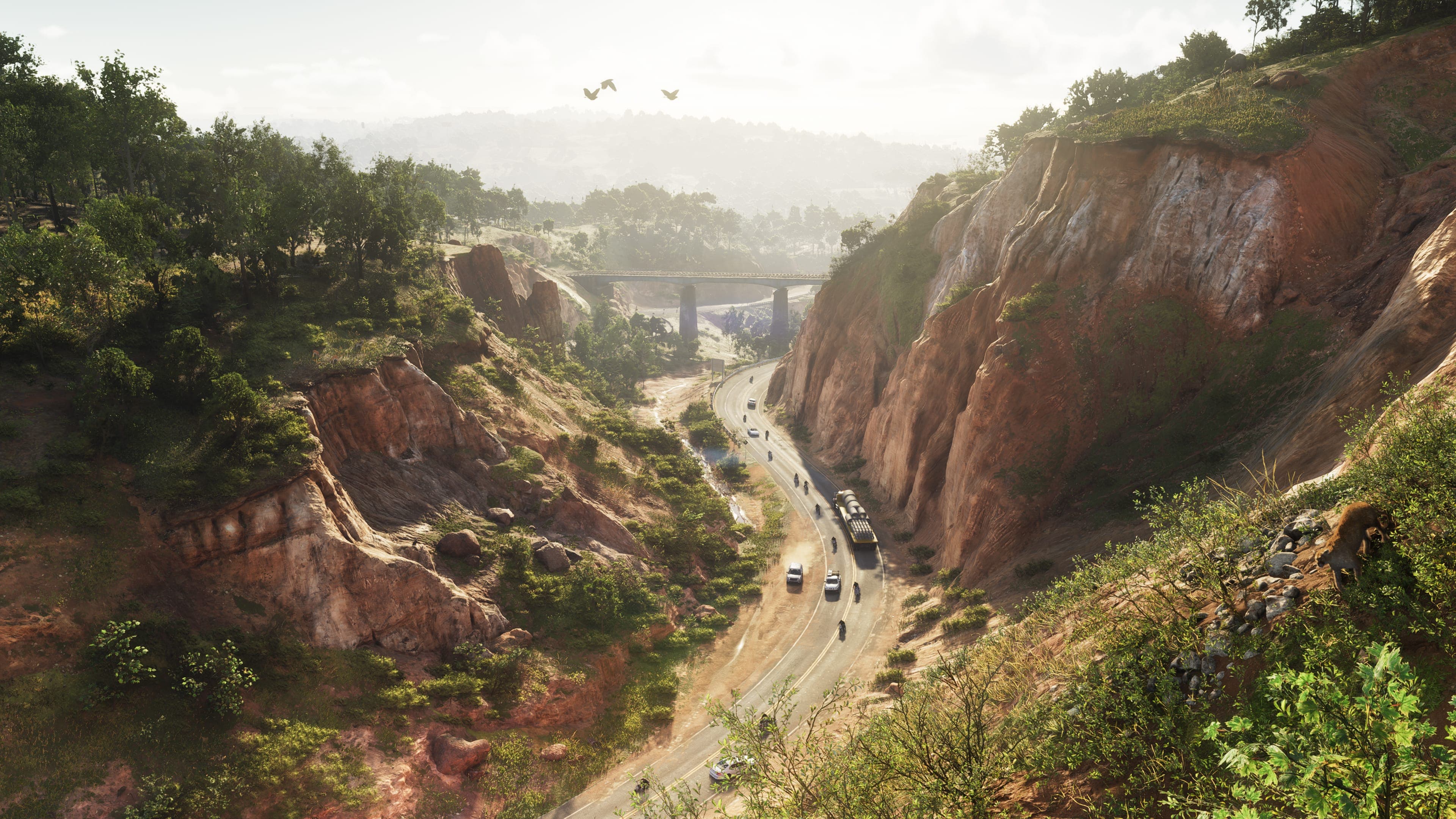 A highway cut into a red rock canyon, traffic winding through the valley below